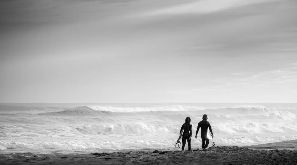 surfing couple holding their boards in black and white photography
